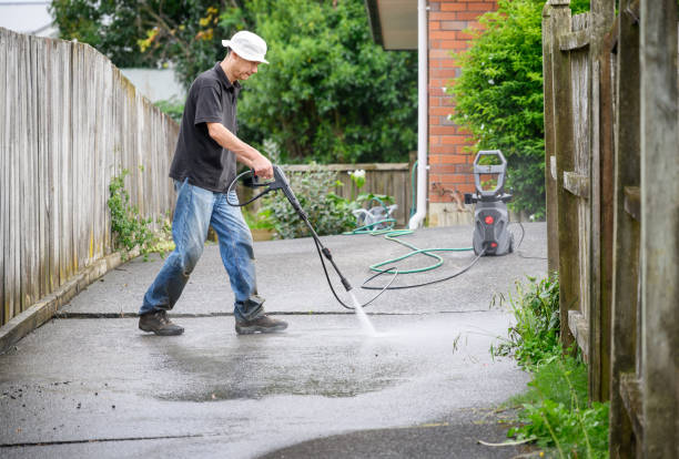 man washing concrete driveway using a pressure washer.